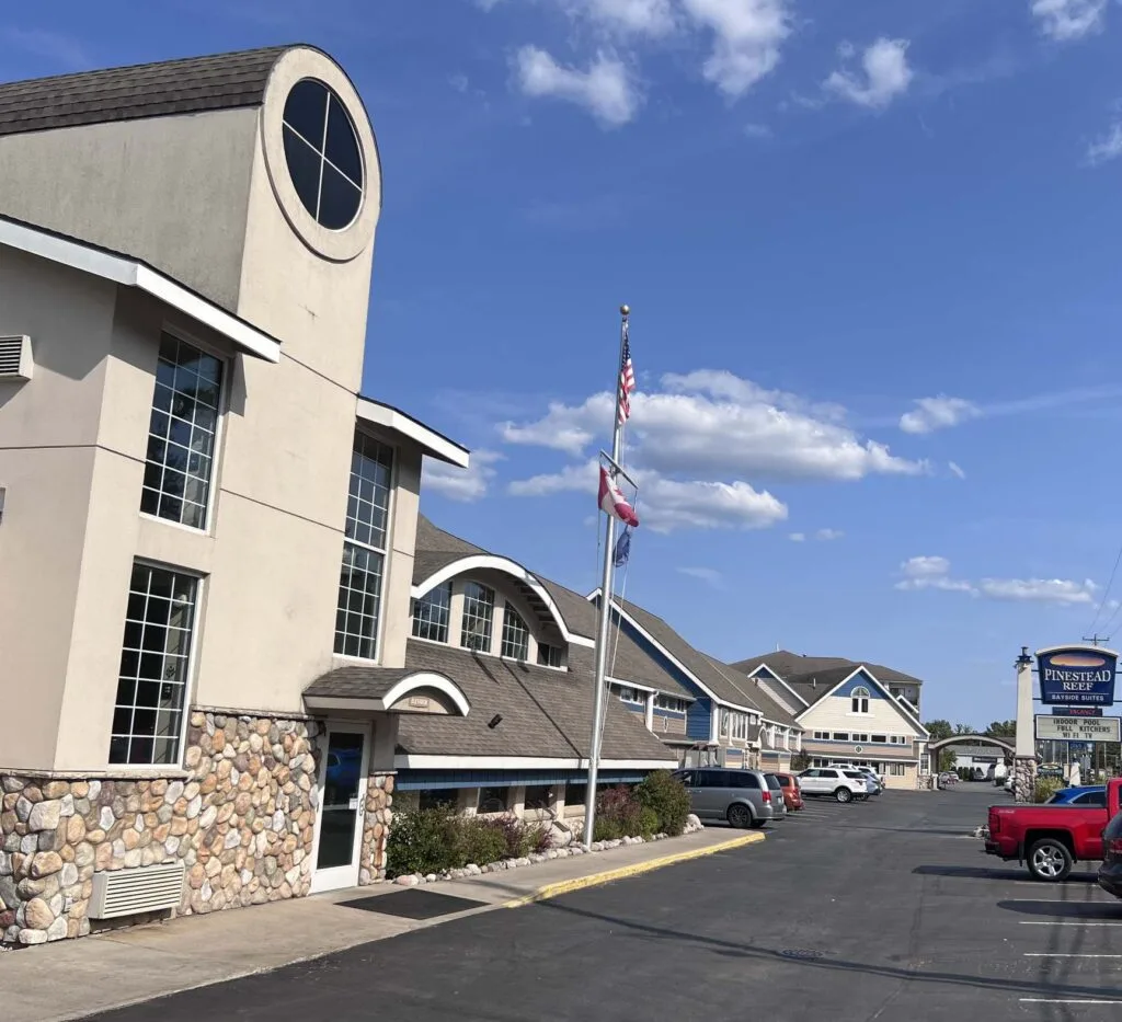 A beige building with stone facade and a flagpole in front of a parking lot