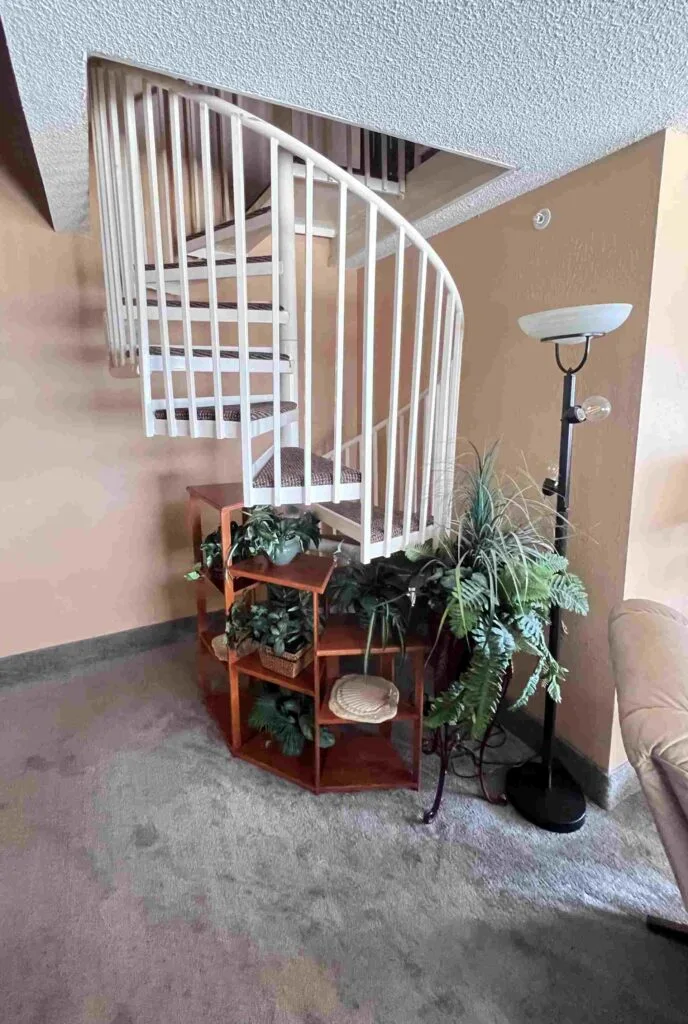 A curved white staircase with a wooden and plant shelf and a floor lamp in a lobby area.